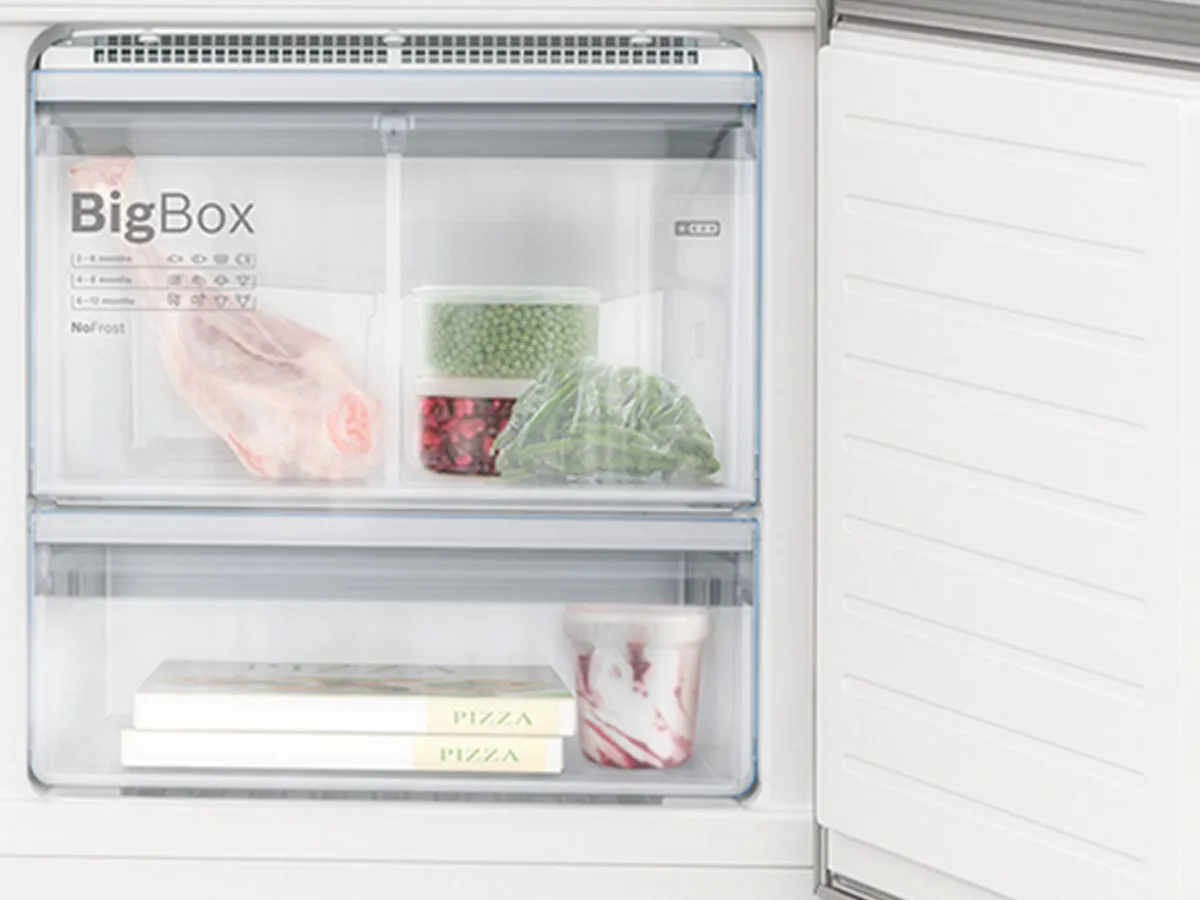 Un intérieur de réfrigérateur propre présentant de la viande, des légumes, des boîtes de pizza surgelées et de la crème glacée, organisés dans des compartiments transparents.
