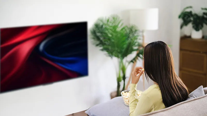Kadın, ekrandaki bitki ve soyut sanat ile oturma odasında TV izliyor.