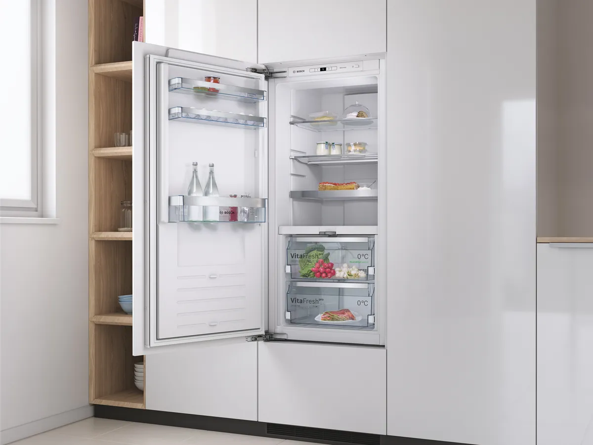 Un réfrigérateur moderne avec une porte ouverte, présentant des étagères remplies de nourriture, de boissons et un bac à légumes transparent, installé dans une cuisine élégante.