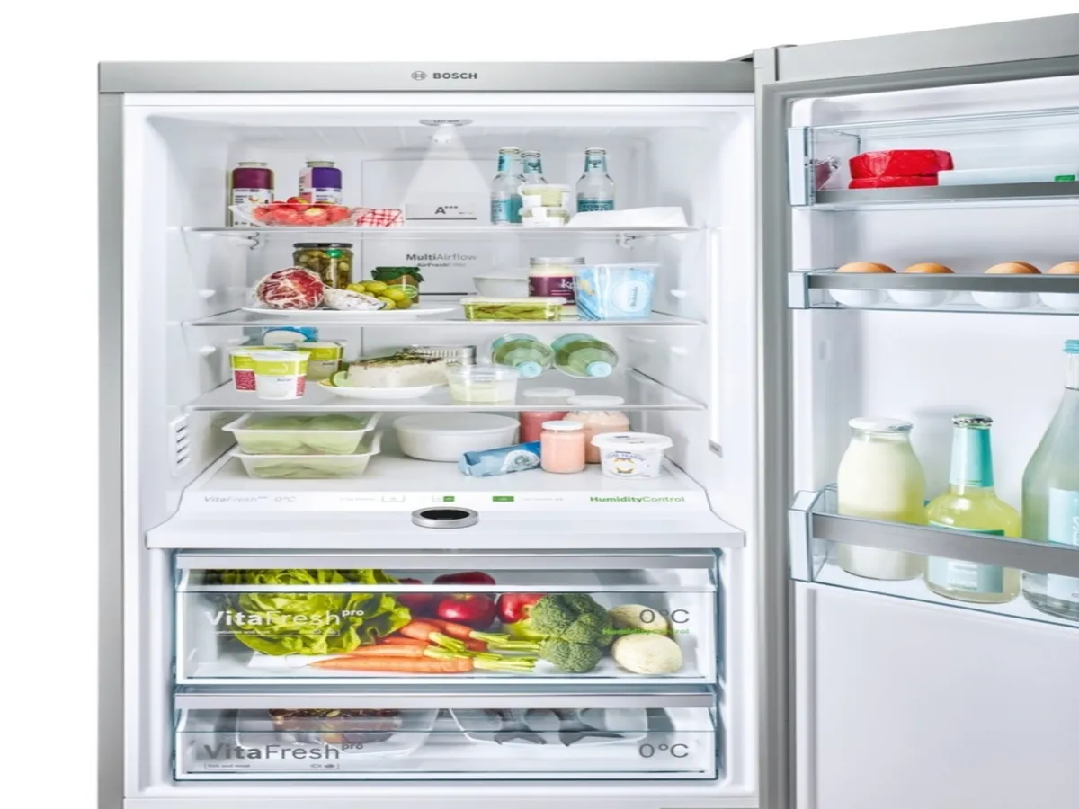 Réfrigérateur Bosch ouvert, bien rempli de légumes, boissons, produits laitiers et condiments.