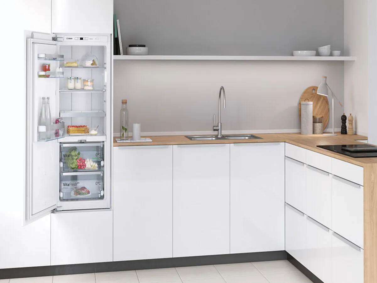 Réfrigérateur encastré Bosch ouvert dans une cuisine blanche moderne en angle avec plan en bois.