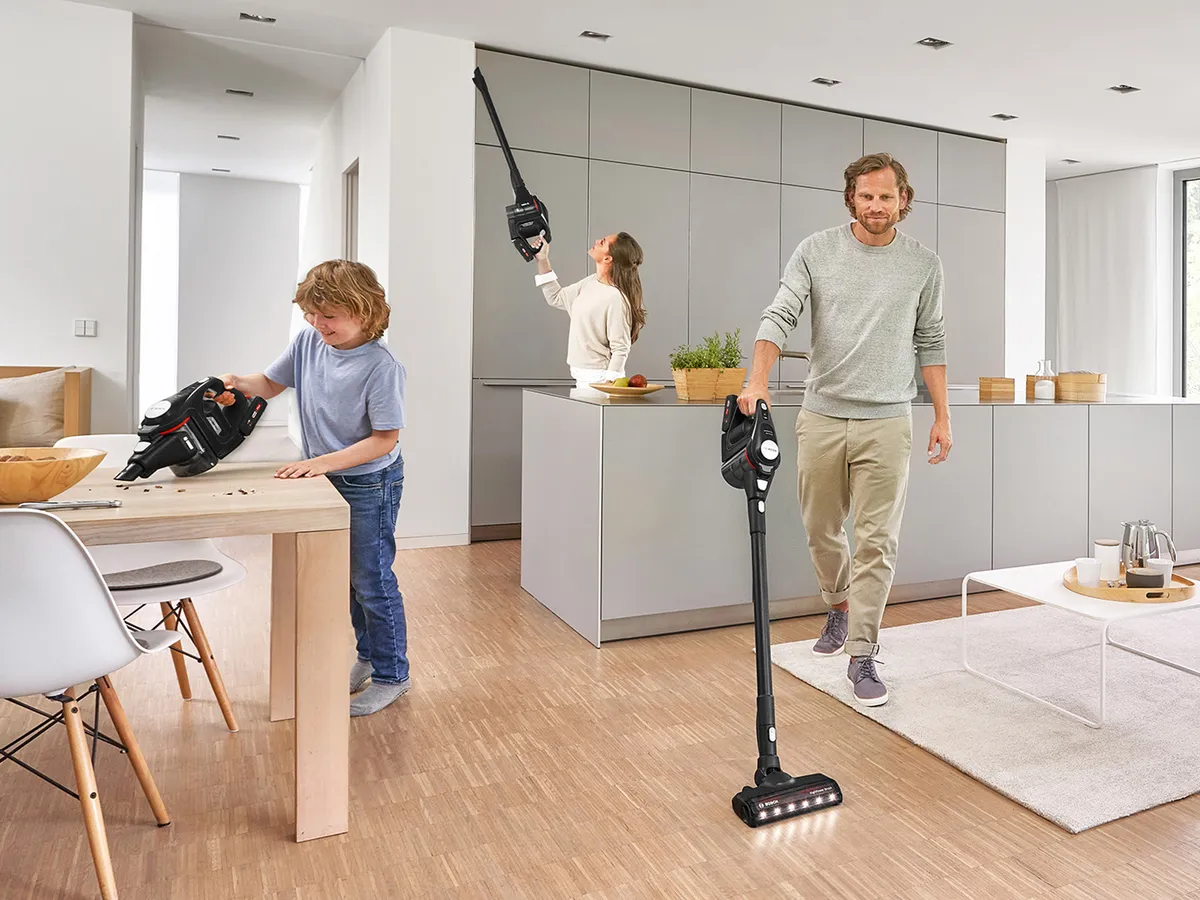 Eine Familie reinigt gemeinsam einen Wohn-/ Essbereich mit dem Bosch Unlimited Akku-Staubsauger.
