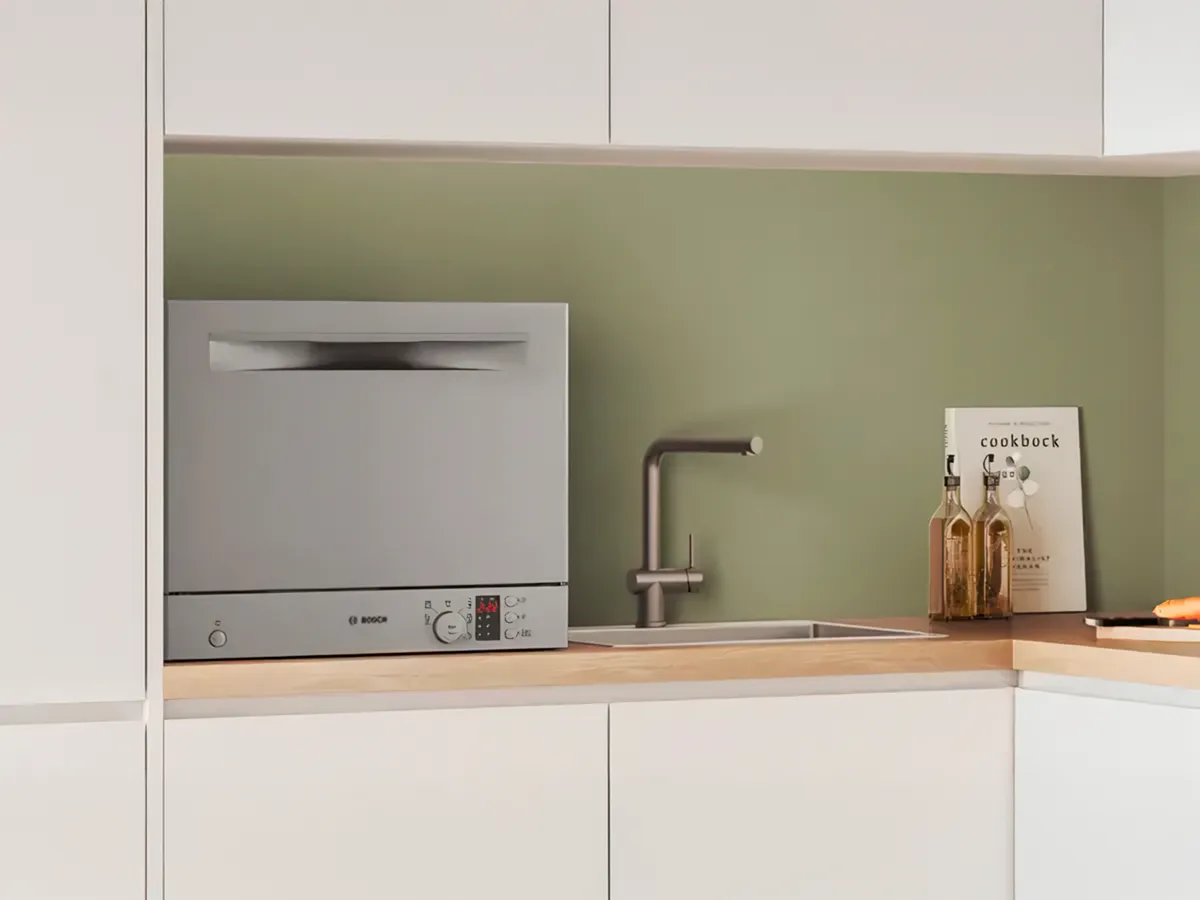 Kompaktne nõudepesumasin asub köögilaual kraani kõrval, pakkudes mugavat ja efektiivset puhastamist väikestes ruumides.