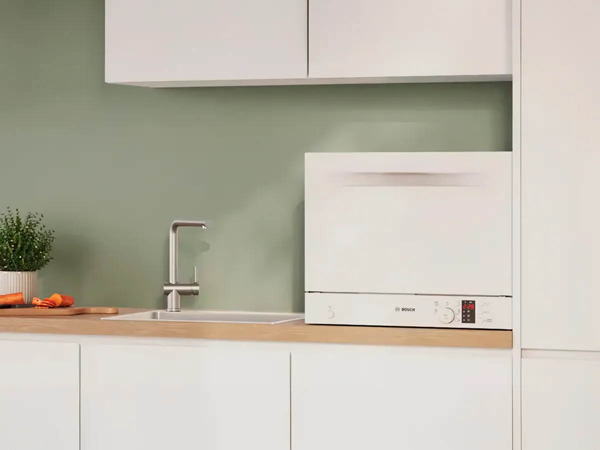 Valge kompaktne eraldiseisev nõudepesumasin tööpinnal, mis on paigutatud valamu lähedale.