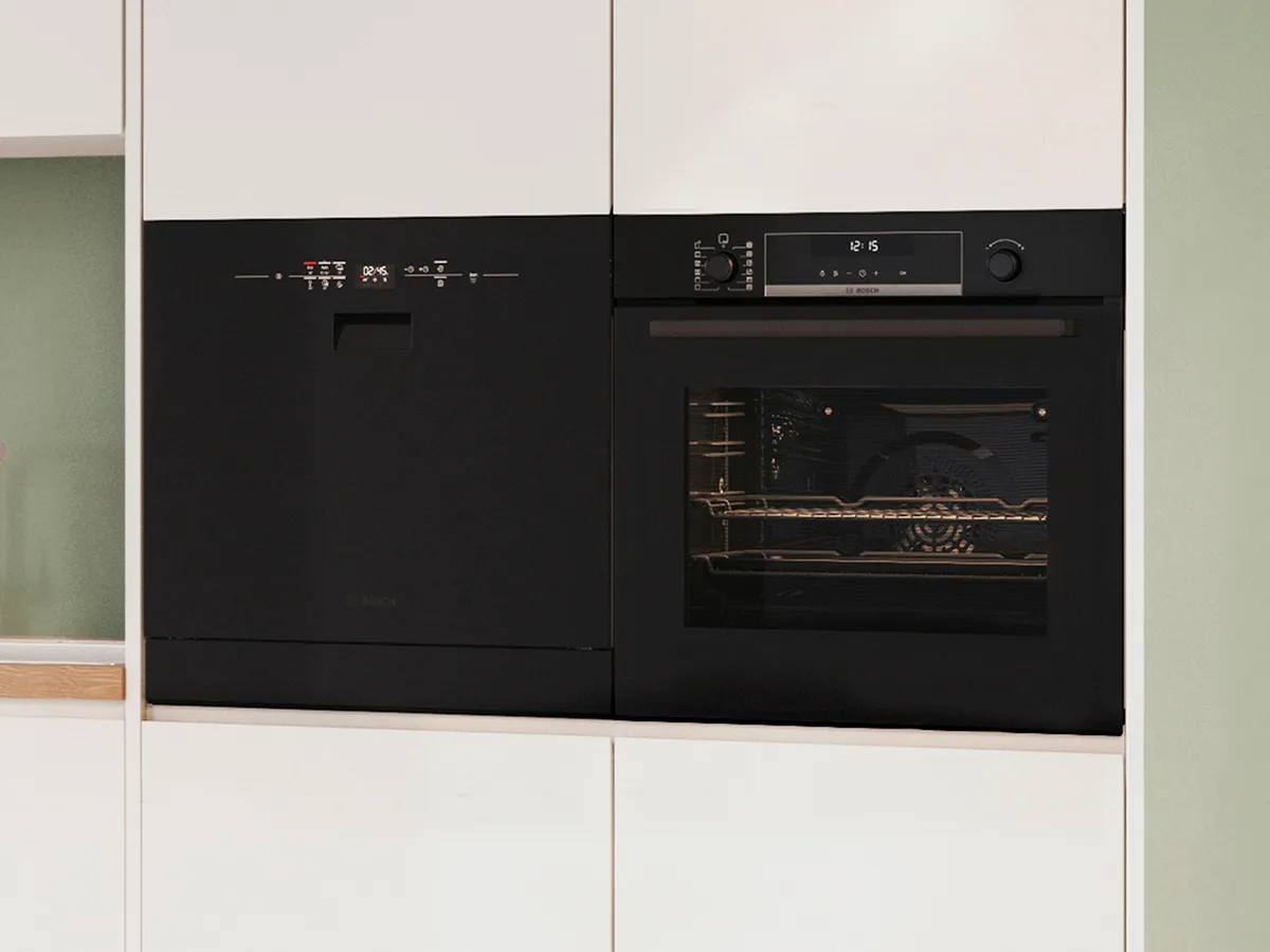 Must nõudepesumasin musta ahju kõrval.