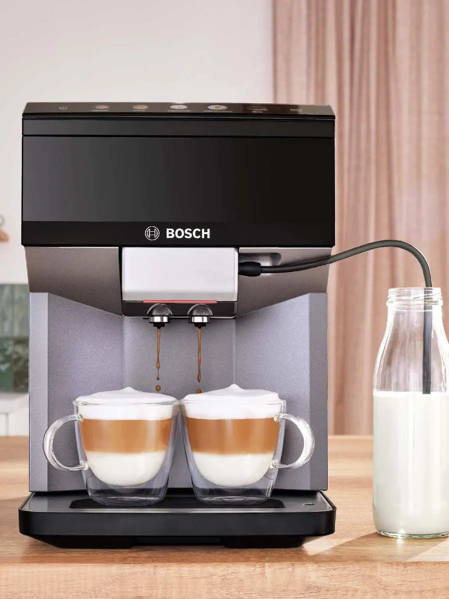 آلة قهوة بوش أوتوماتيكية بالكامل تصنع كوبين من القهوة بالحليب الرغوي، مع زجاجة حليب بجانبها. 