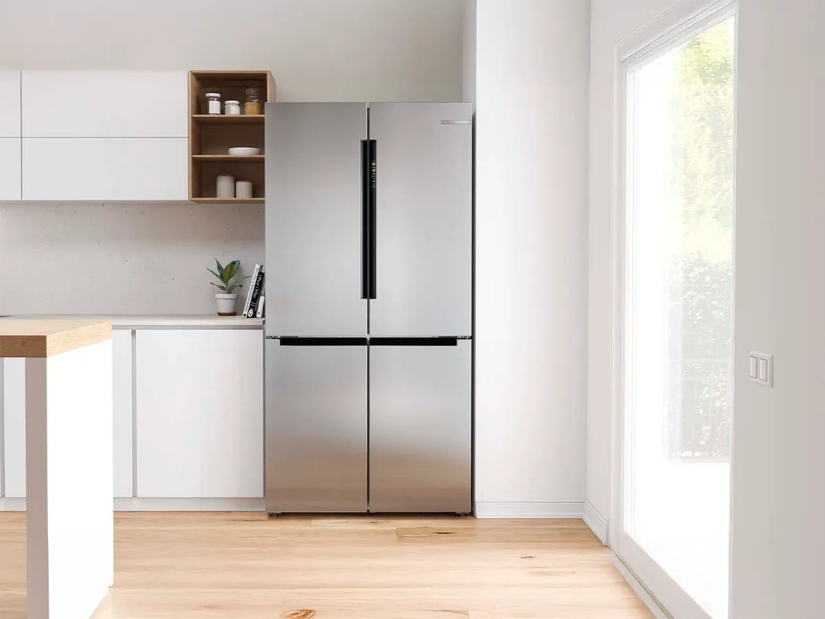 Frigorífico de portas francesas com barras de manuseio pretas ao lado de uma janela numa cozinha aberta.