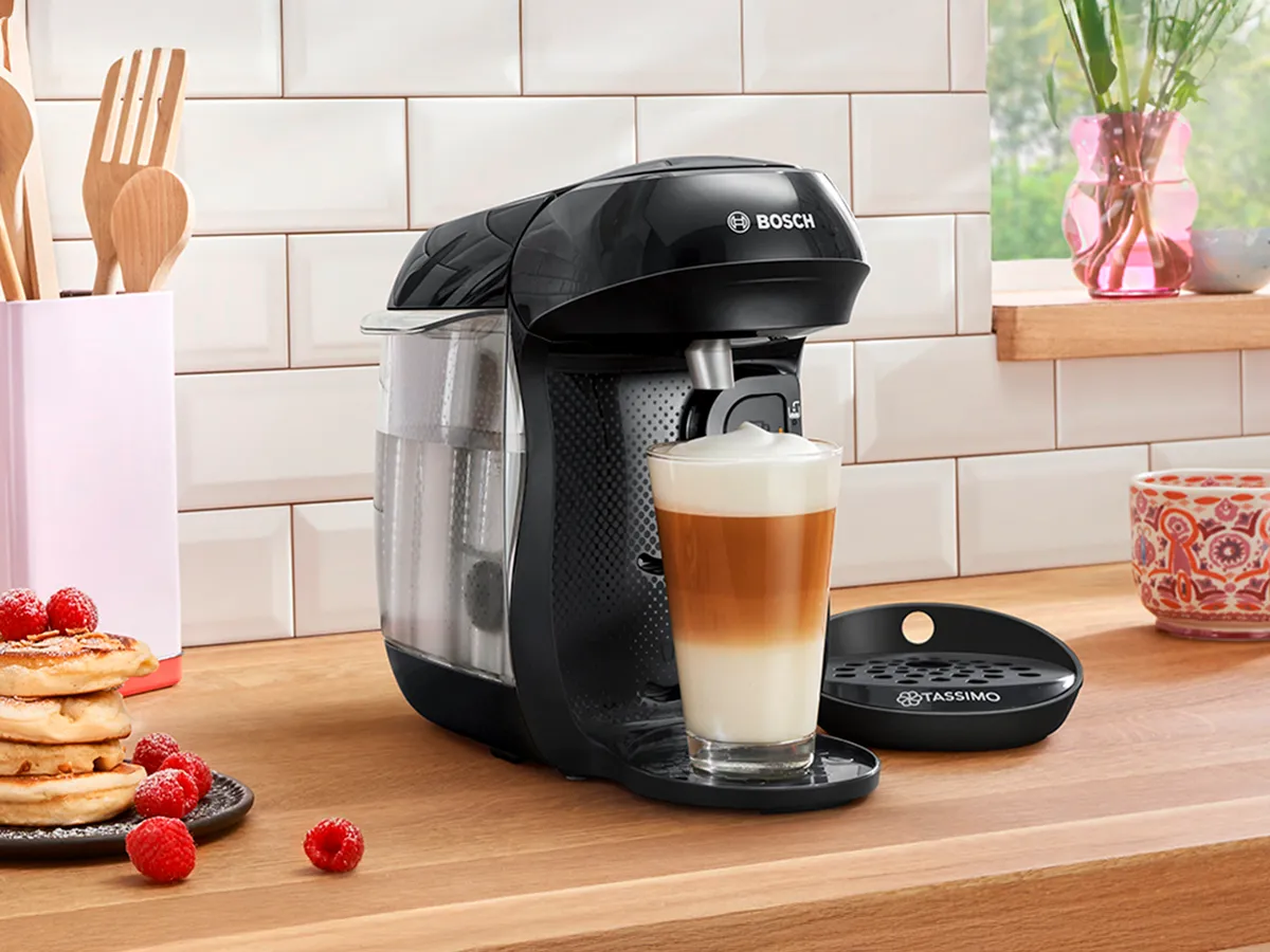 TASSIMO HAPPY friendly brewing a Latte Macchiato on a kitchen worktop and a plate of pancakes next to it.