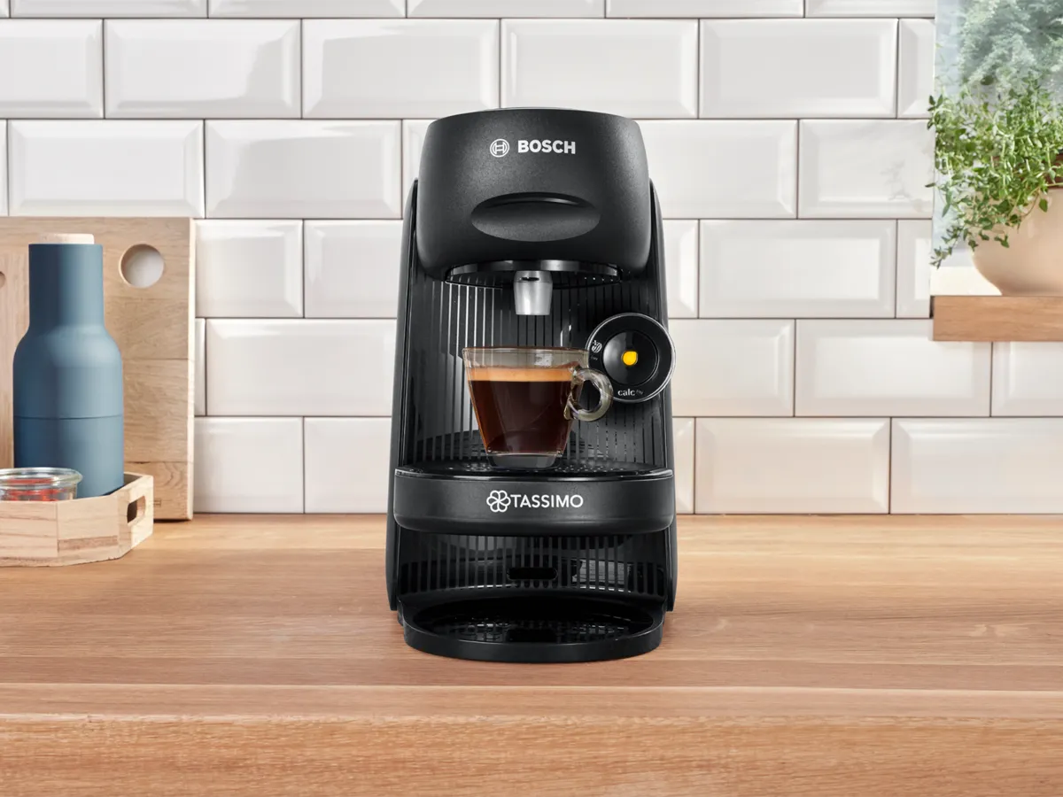 The coffee machine TASSIMO FINESSE friendly on a kitchen worktop with a filled expresso cup.