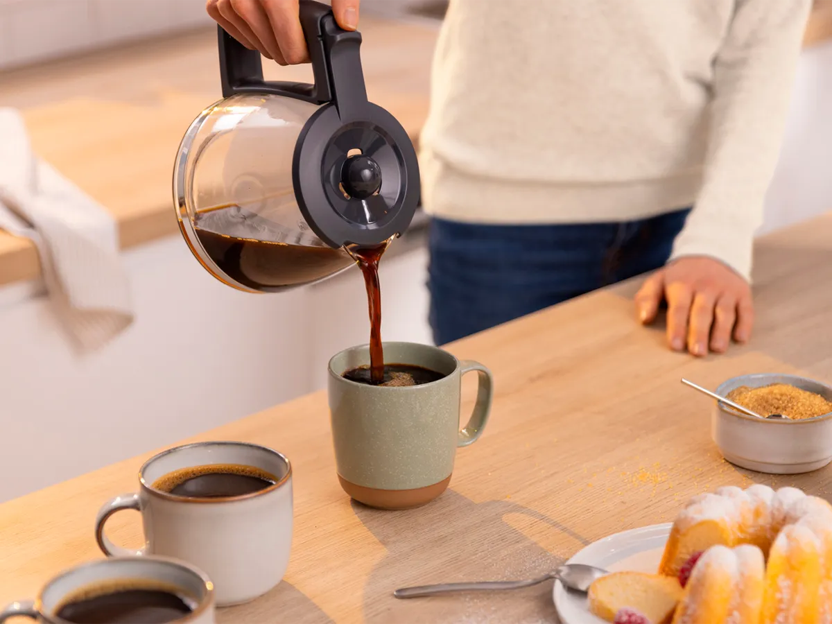 Pessoa a verter café numa chávena a partir de uma cafeteira de jarra de vidro.