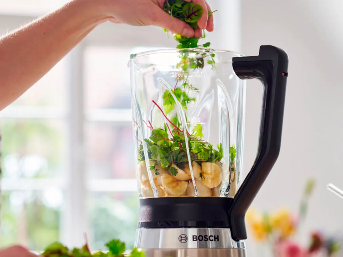 Liquidificador Bosch cheio de bananas e ervas frescas, perfeito para fazer smoothies saudáveis e misturas nutritivas em casa.