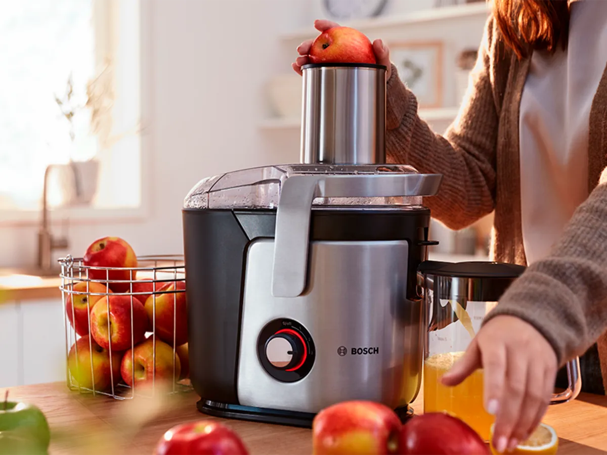 A person standing at a kitchen worktop puts apples into a Bosch juicer.