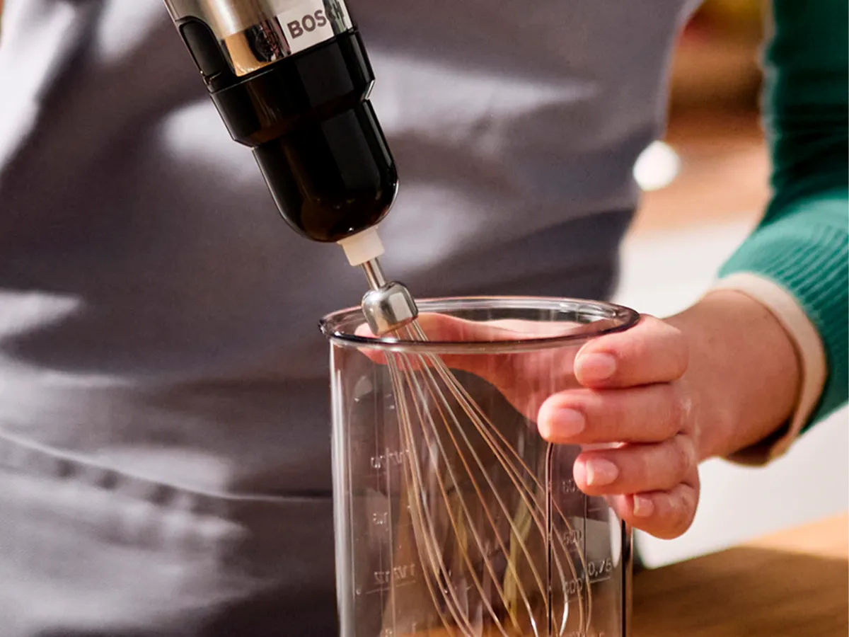 Alguém está prestes a usar um liquidificador de mão com um batedor para bater claras de ovo em um copo.