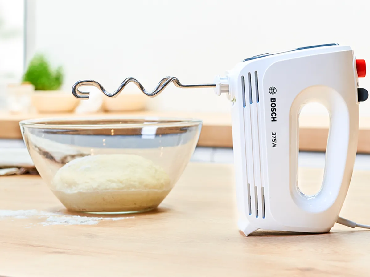 Liquidificador de mão CleverMixx com acessório de gancho para massa, amassando a massa com facilidade em uma tigela de vidro para a perfeita experiência de panificação caseira.