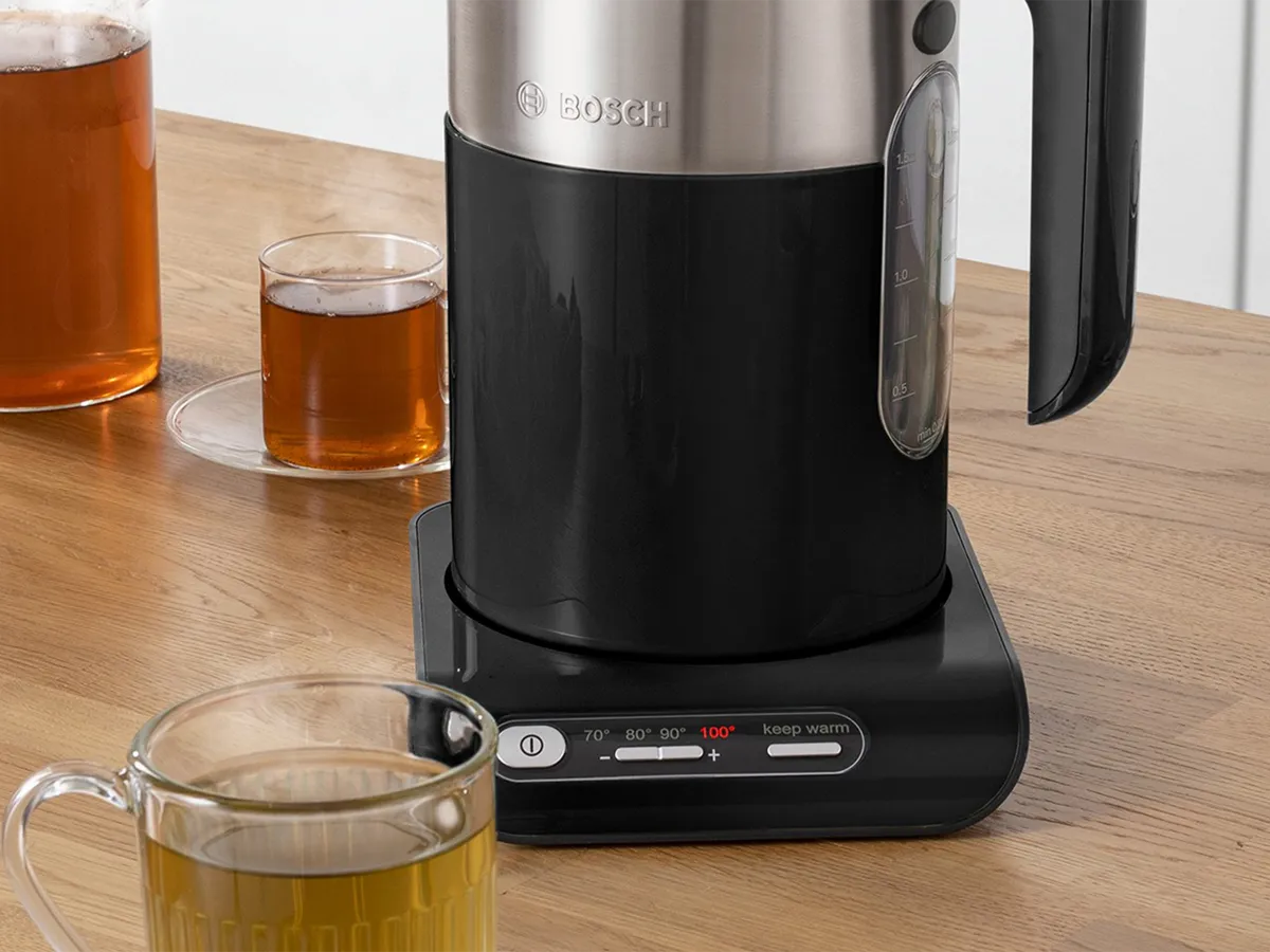 Chaleira Styline em preto e aço inoxidável sobre uma bancada de cozinha ao lado de uma seleção de bebidas quentes em copos.