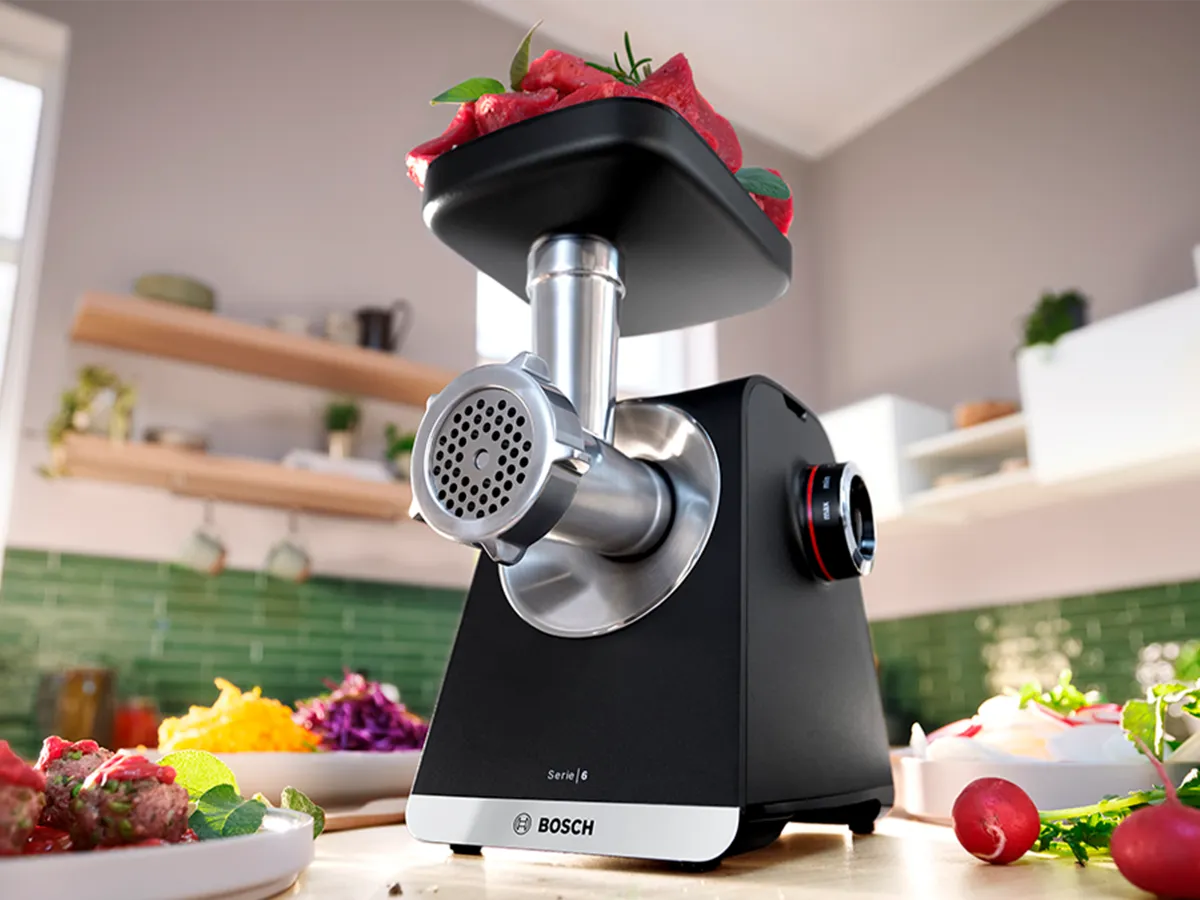 MultiPower Serie 6 com acessório de picador de carne em uma bandeja sobre a bancada da cozinha, ao lado de um prato com pedaços de carne.