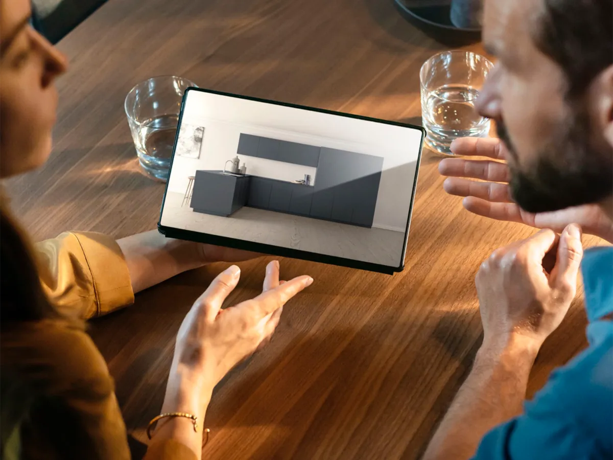 Um homem e uma mulher sentados à mesa a discutir um design de cozinha exibido num tablet inteligente.