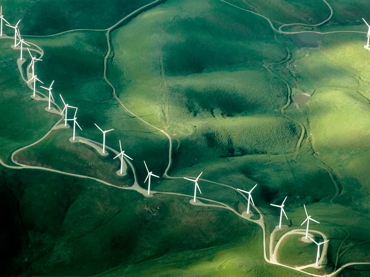 Aerial view of a wind farm with turbines on rolling green hills, symbolising renewable energy and sustainability.