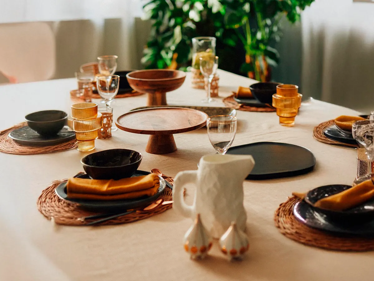 Beautifully set dining table with elegant tableware, wooden serving stands, and glassware in a warmly lit space.