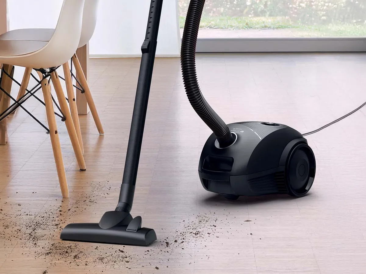 En cylinderdammsugare med påse suger upp synlig smuts från golvet.