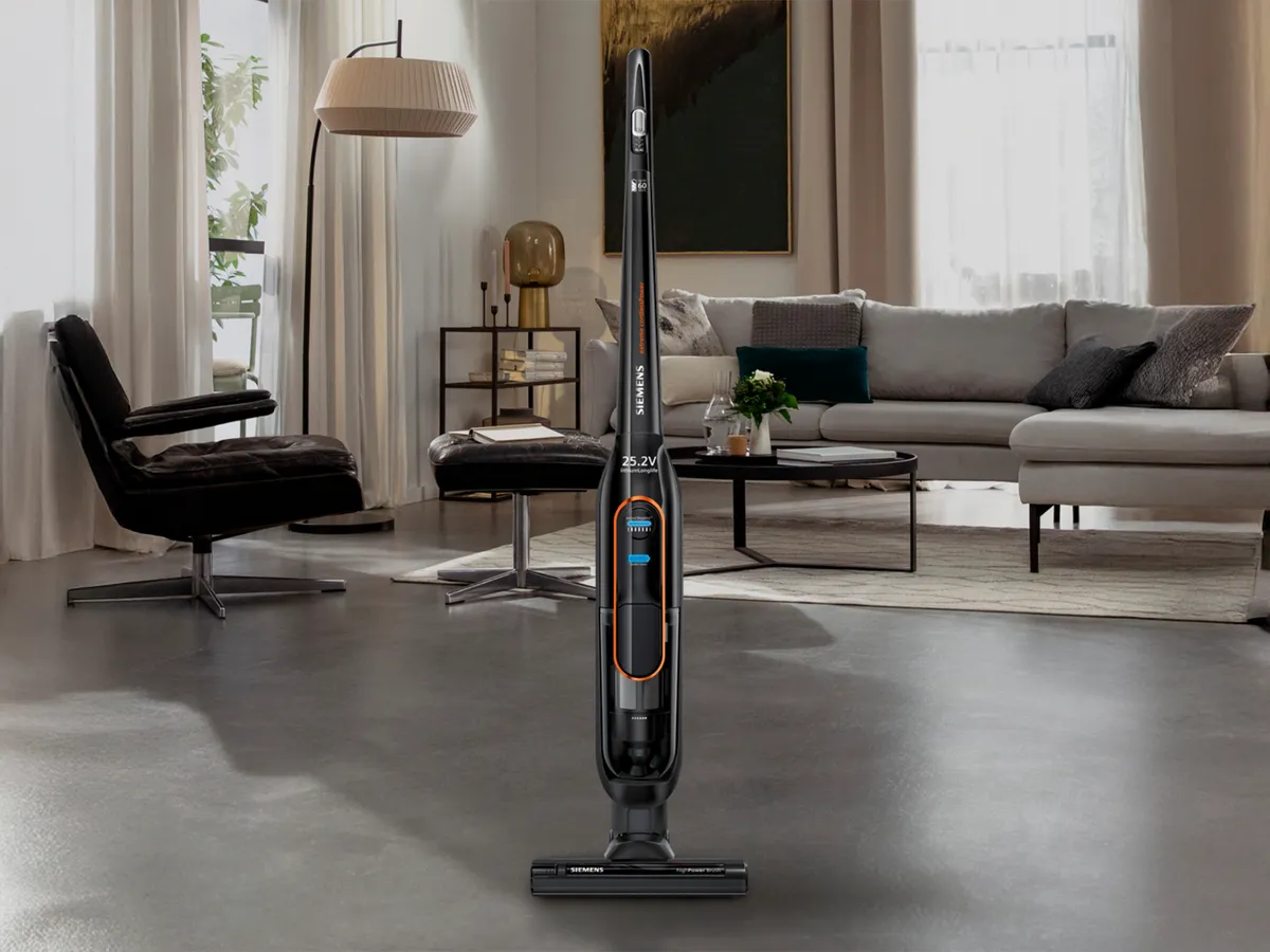 A cordless vacuum cleaner standing upright in a modern living room setting.