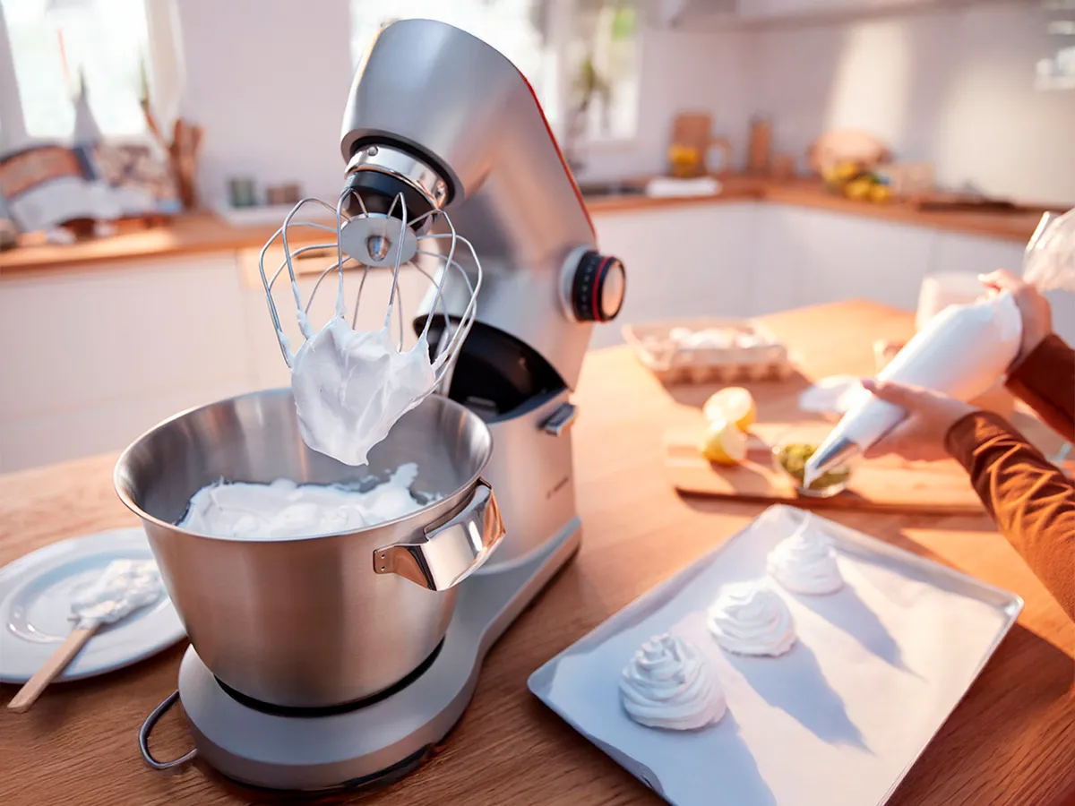 Misturador de cozinha chicoteando creme em contador de madeira com ingredientes de cozimento. 