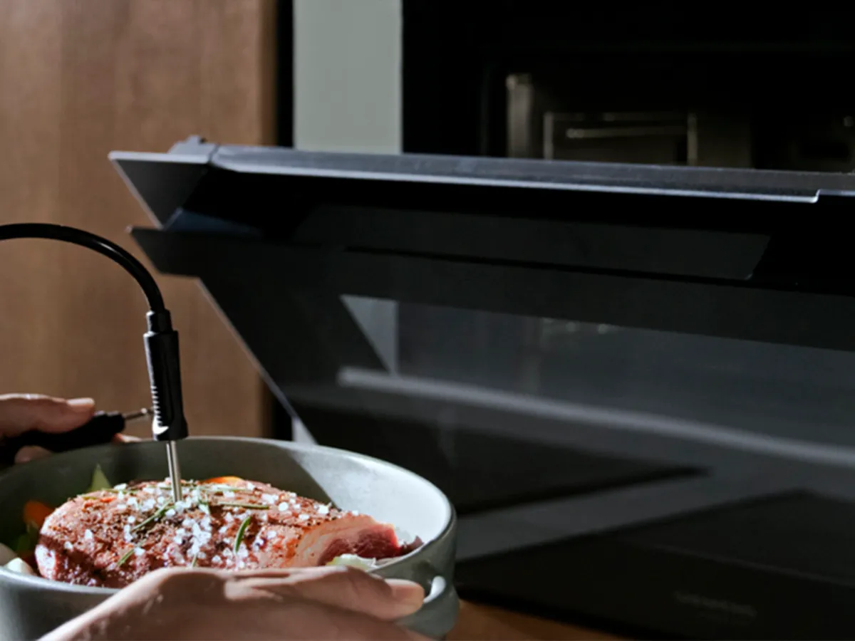 Uma mão que interage com um ecrã tátil elegante num forno moderno, selecionando a opção Individual Browning para cozinhar.