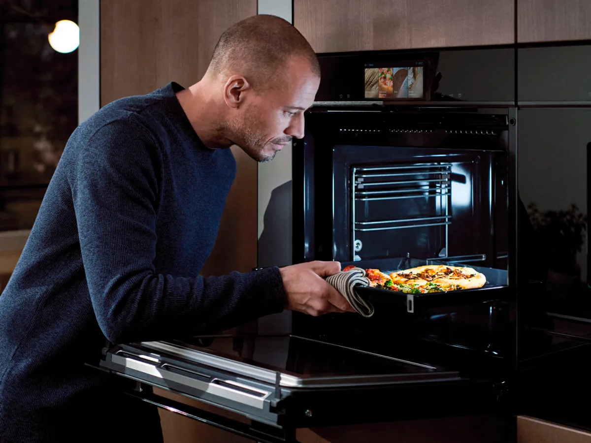 Pessoa a usar luvas de forno para tirar uma piza do forno.