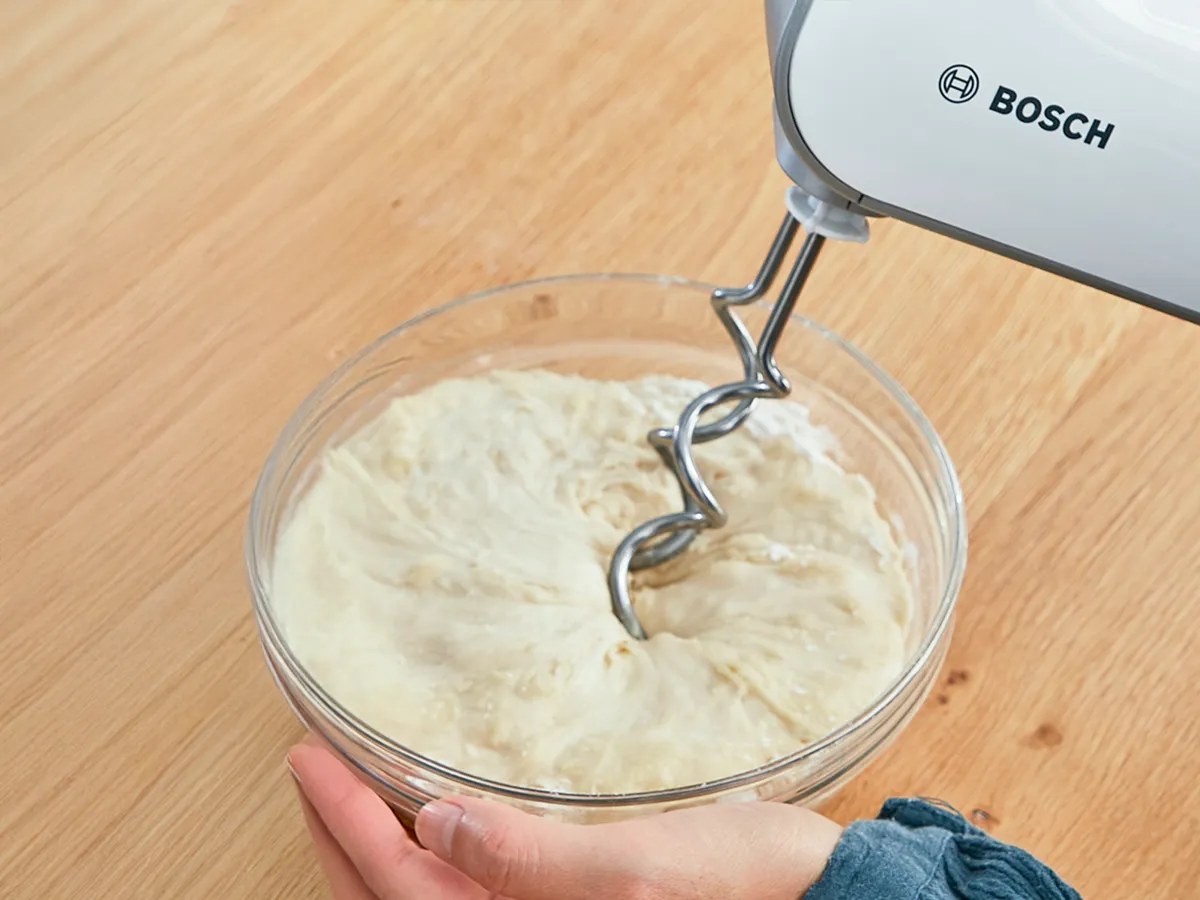 Uma pessoa amassando a massa com o liquidificador de mão Bosch.