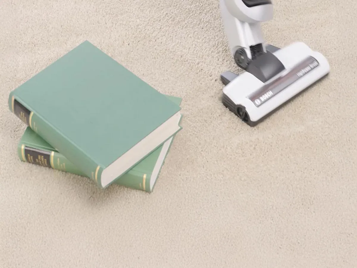 A vacuum cleaner vacuums a carpet. There are books beside it.