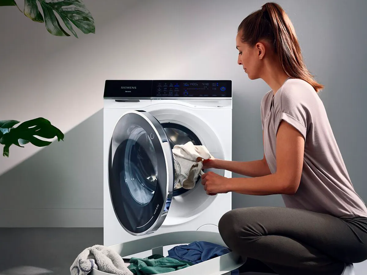 A person loading laundry into a Siemens front-loading washing machine.