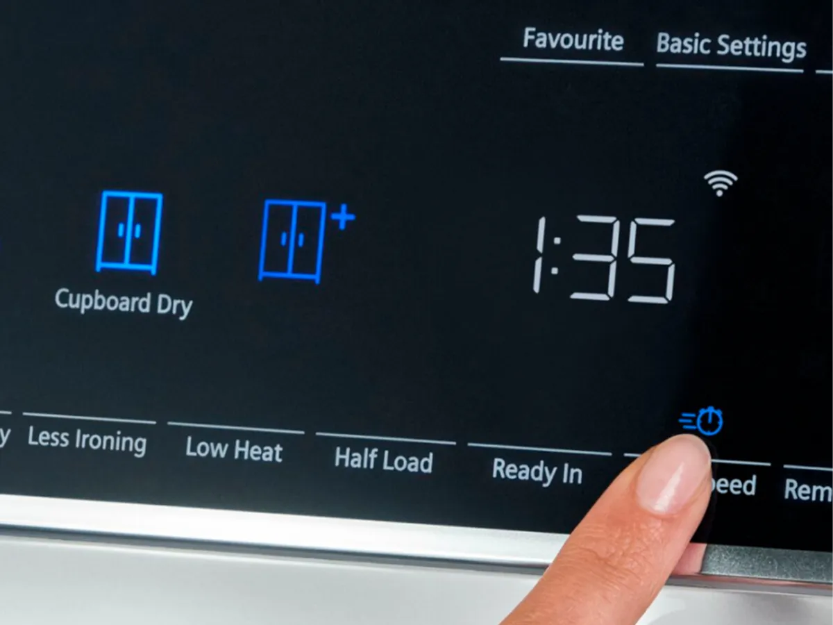 A finger pressing a button on a dryer's digital interface displaying settings and time.