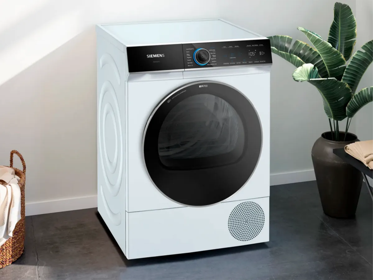 Uma máquina de lavar Siemens moderna numa sala com uma planta e um cesto de vime.