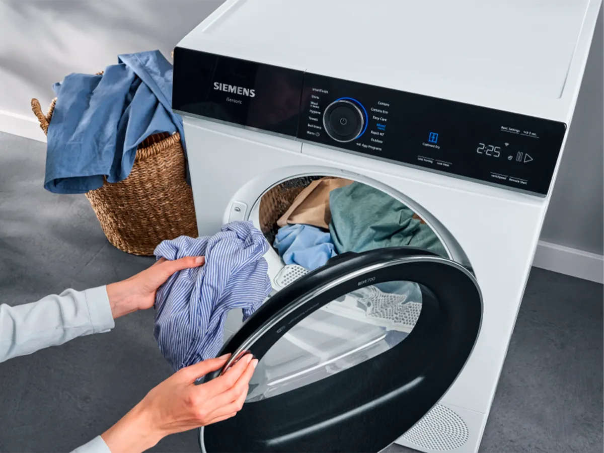 Pessoa a carregar uma máquina de lavar Siemens com roupas.