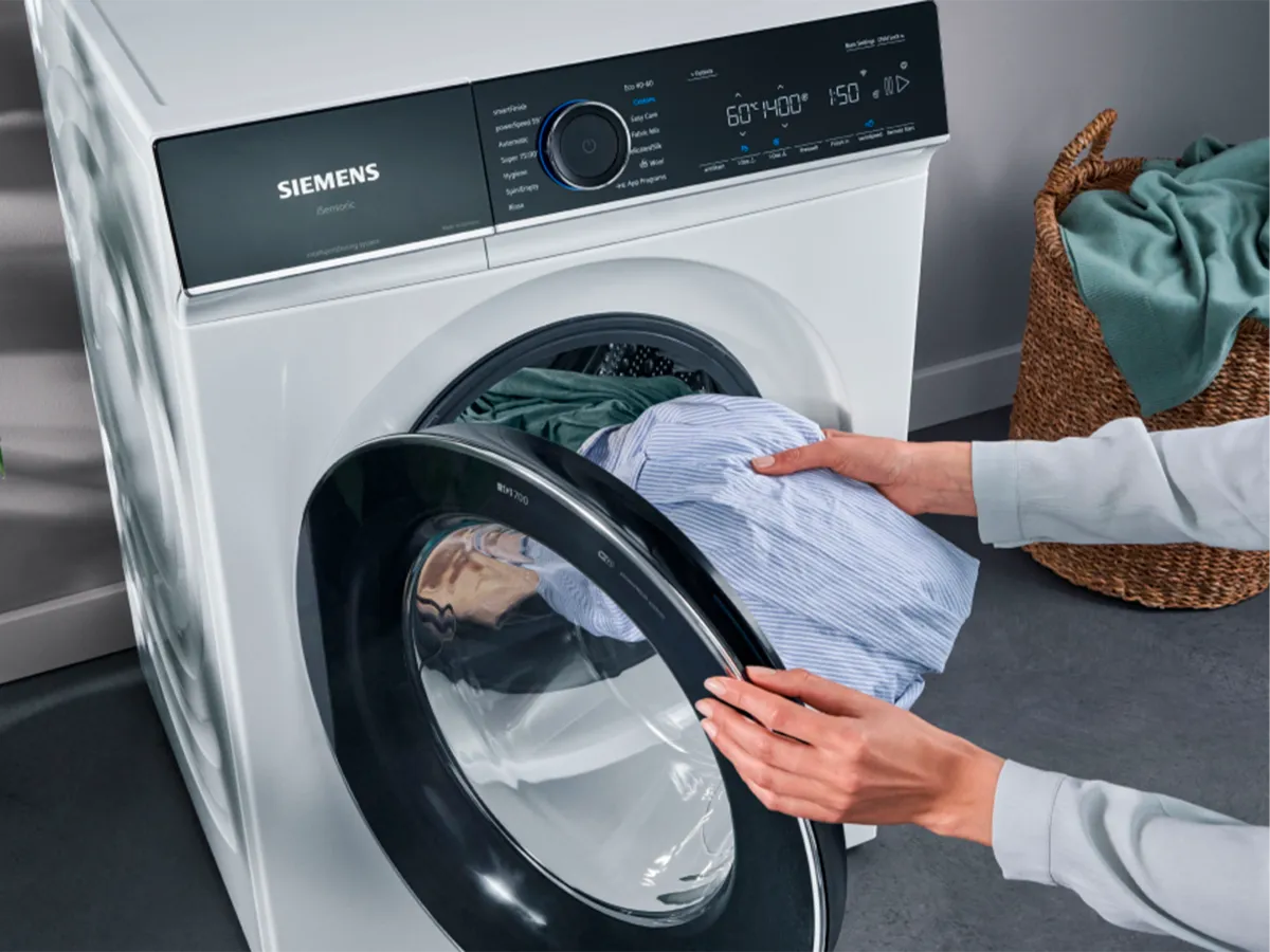 Pessoa a carregar roupas numa máquina de lavar Siemens.