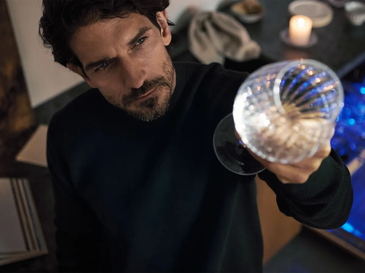 Pessoa segurando um objeto de vidro esférico com reflexos de luz, próximo a um livro aberto e uma vela.