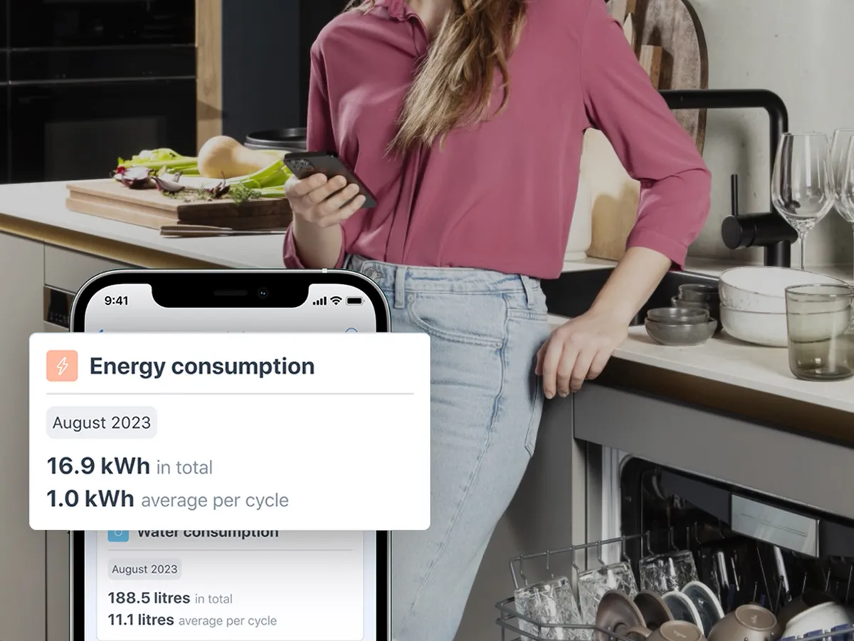 Person som håller i en telefon med statistik över energiförbrukning i ett kök.
