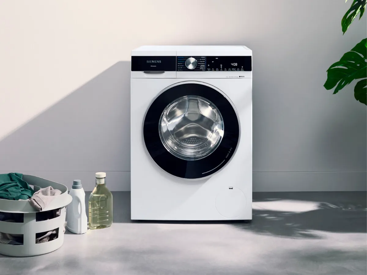 Front-loading washing machine with detergents and laundry basket in a well-lit room.