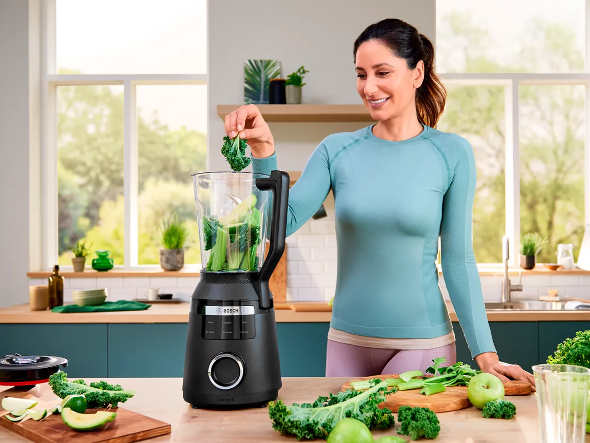 Uma mulher preenchendo o liquidificador VitaPower com legumes verdes.