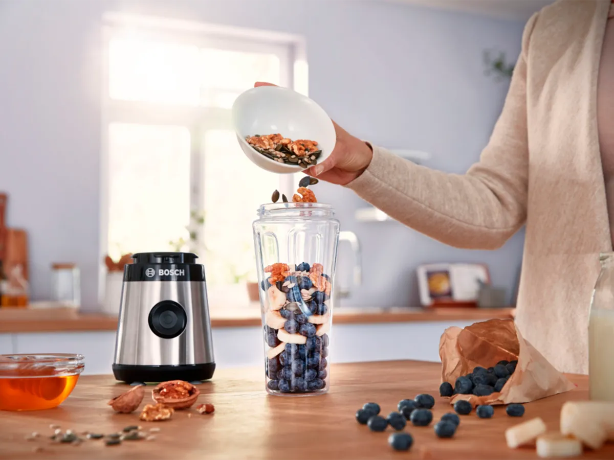 Uma mulher colocando frutas e nozes no liquidificador mini VitaPower Serie 2 da Bosch.