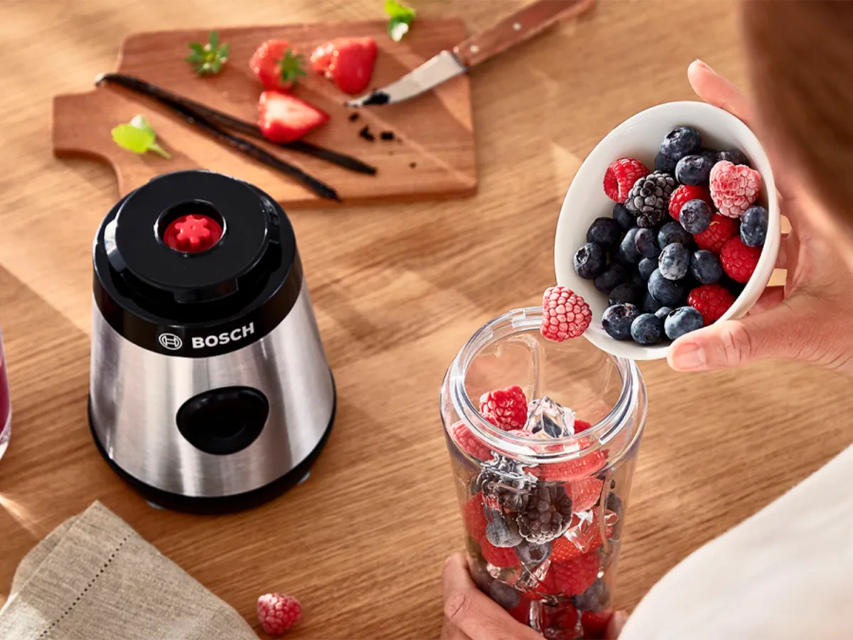 Uma mulher colocando frutas congeladas na garrafa do liquidificador mini VitaPower Serie 2 da Bosch.