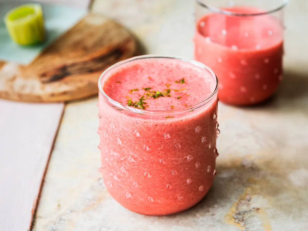 Copo de smoothie vermelho decorado com raspas de limão, colocado sobre uma mesa rústica ao lado de outro copo.