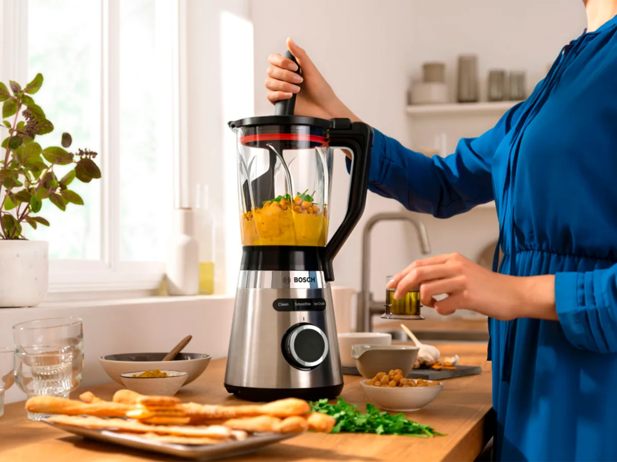 Uma pessoa usando um liquidificador Bosch com um empurrador para preparar um smoothie fresco com grão-de-bico.