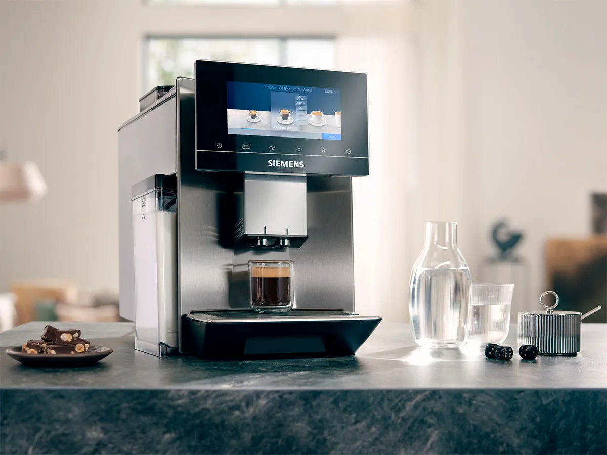 EQ900 espresso-/kaffemaskine står på en granitbordplade, ved siden af vandkaraffel, bagværk og en sukkerskål.