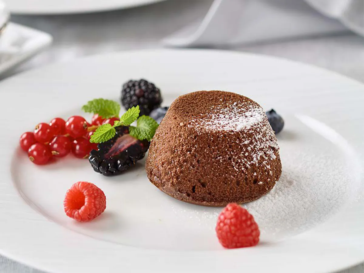 Chocolate lava cake dusted with powdered sugar, served with fresh berries and mint on a white plate.