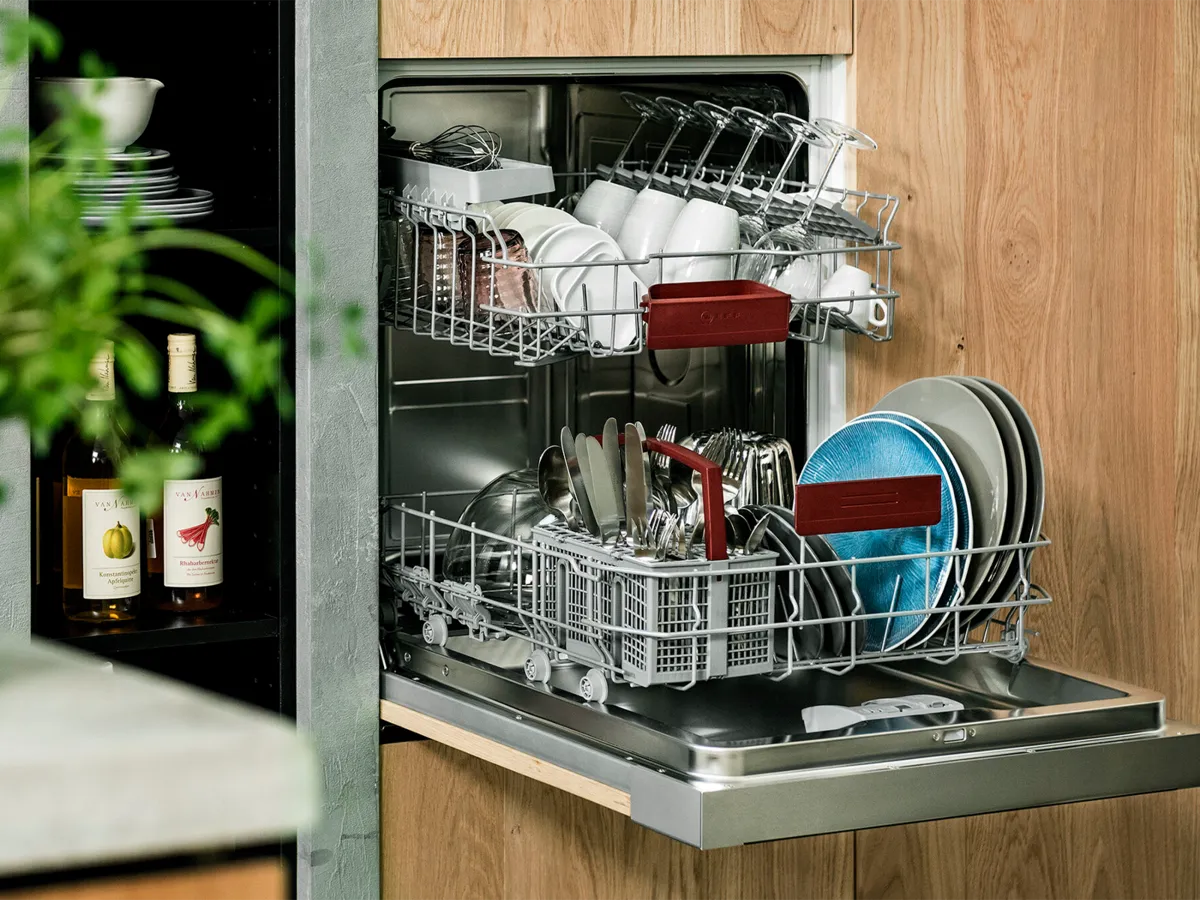 A 60 cm dishwasher with an open door incorporated at a comfortable height in a light-brown kitchen cabinet