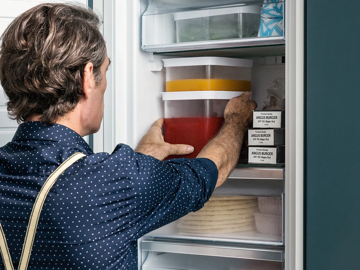 A man placing storage containers with food into a freezer on shoulder-height.