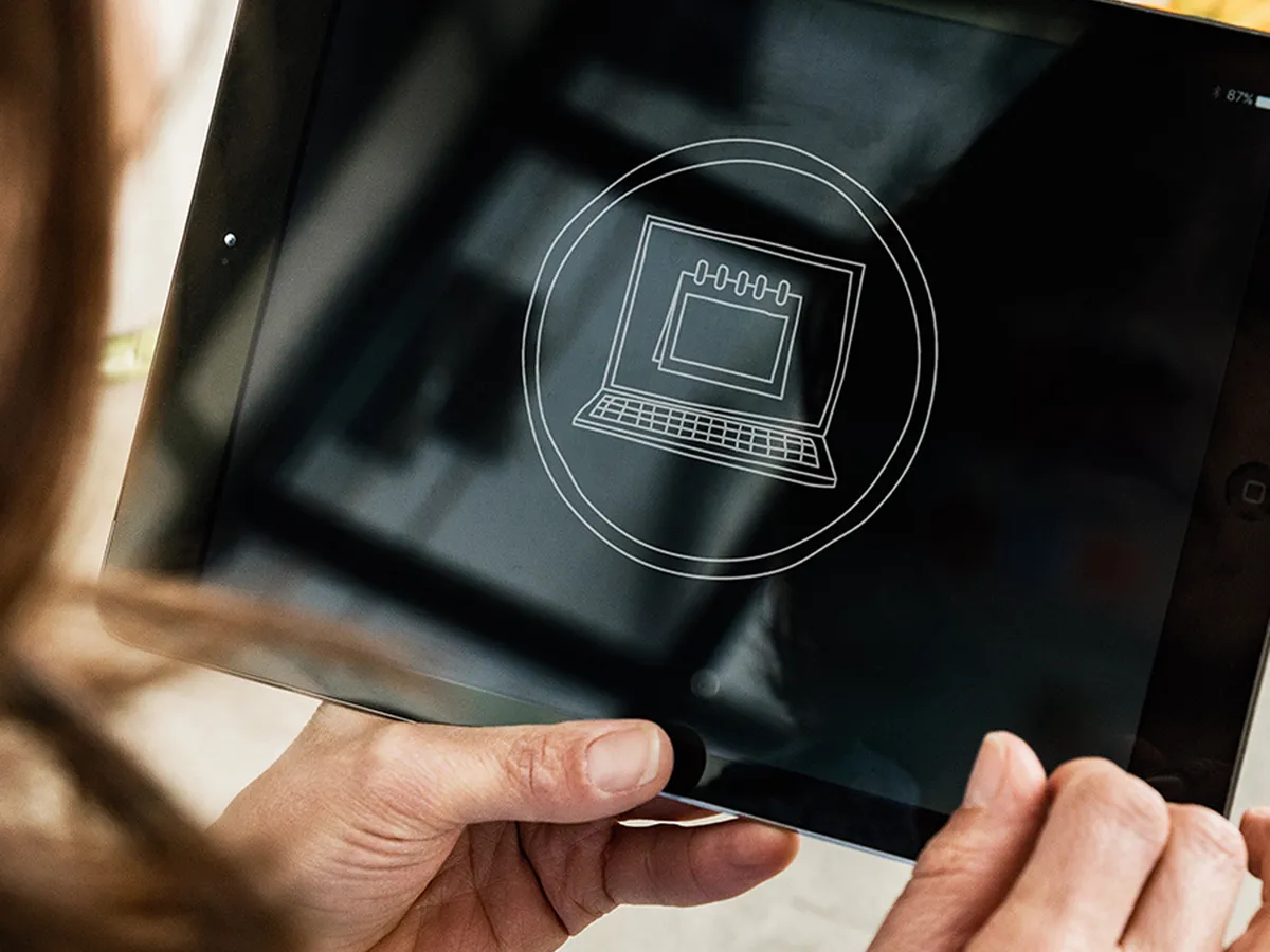 Person holding a tablet displaying a laptop icon, with vegetables in the background.
