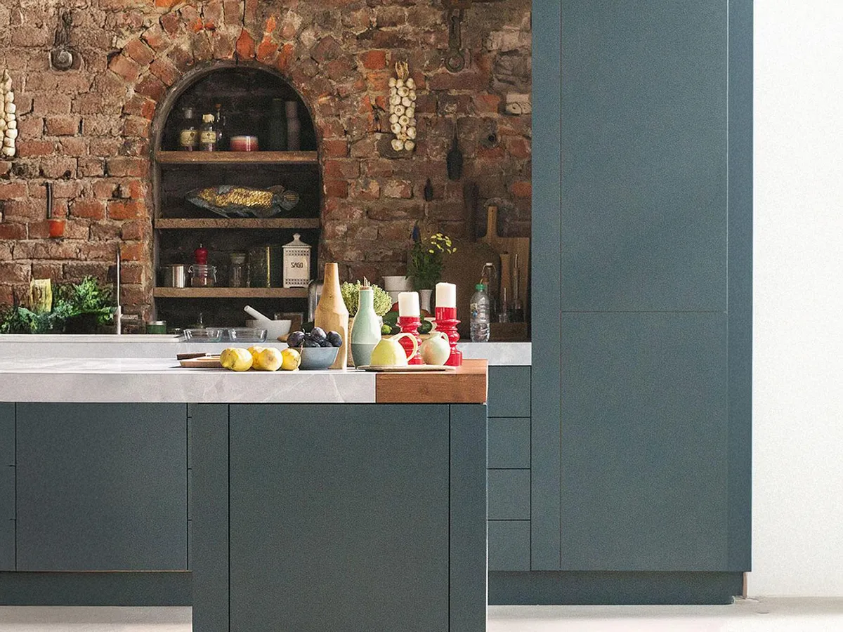 Modern kitchen with teal cabinets, exposed brick wall, and a wooden countertop with utensils.