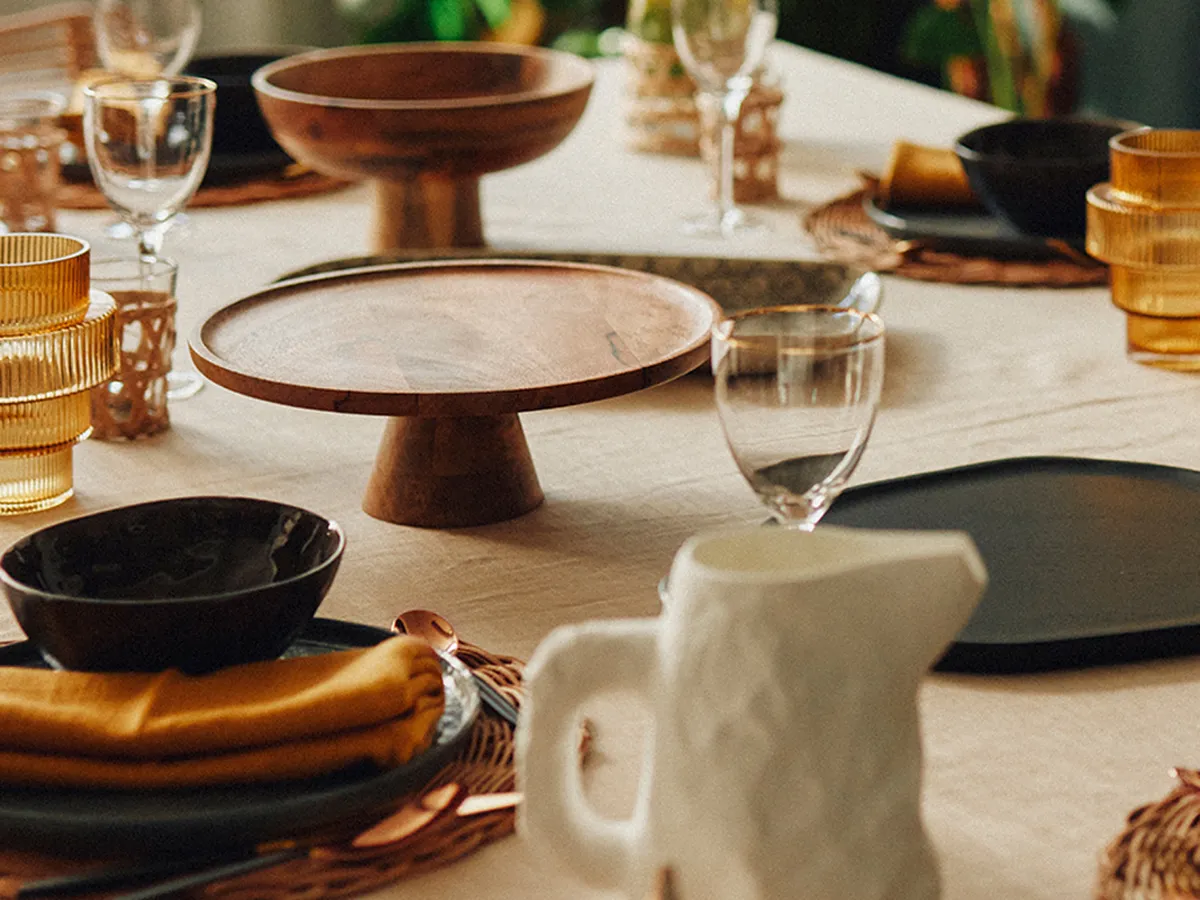 Tischszene mit Leinentischdecke, Weingläsern, Keramik-Etageren und orangenen Glasvasen.